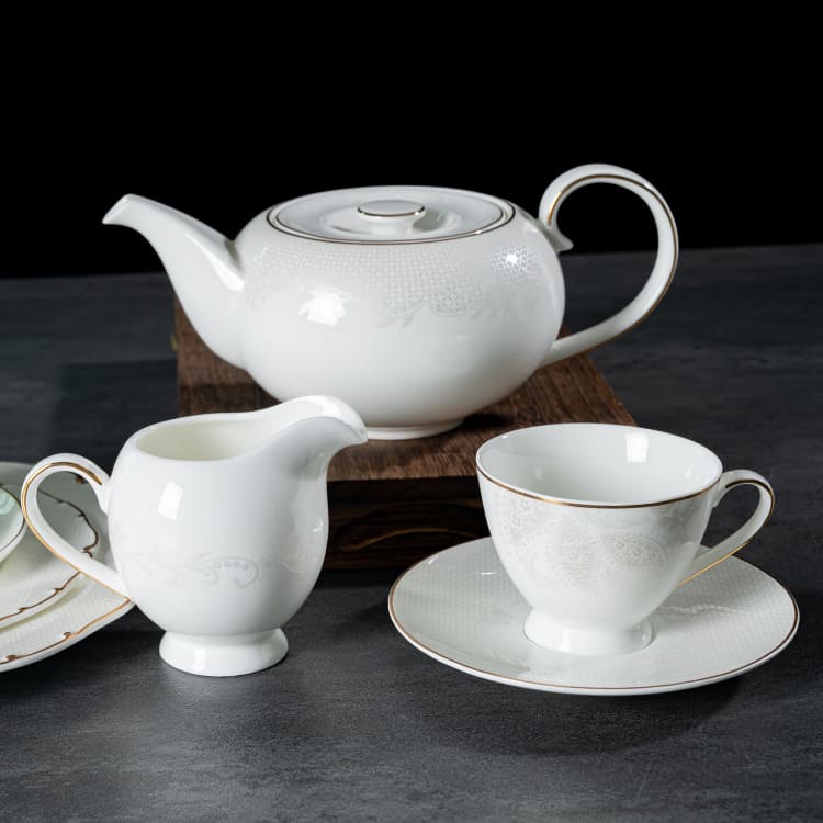A refined bone china tea set with floral patterns and gold rims, including a teapot, creamer, and teacup with saucer.