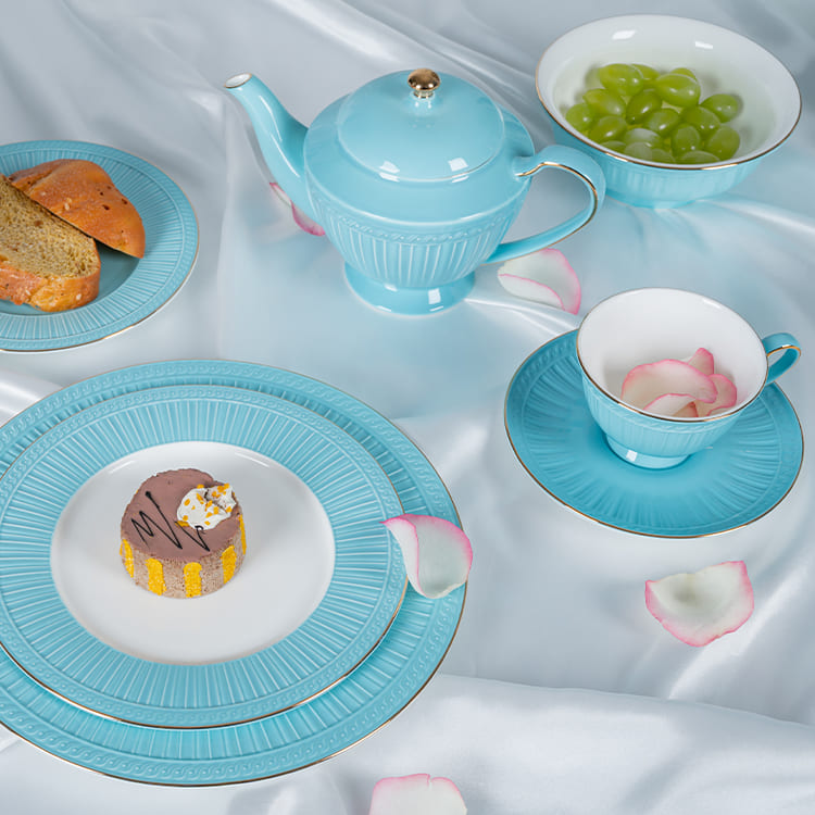This image presents a luxurious tea setting featuring a blue bone china dinnerware set. The arrangement includes a teapot, a cup, saucers, and plates, all showcasing a delicate blue glaze with intricate patterns.