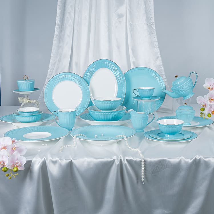 This image showcases an exquisite blue bone china dinnerware set, elegantly arranged on a pristine white satin tablecloth. The set includes a variety of plates, cups, saucers, and a teapot, all featuring a delicate blue glaze with intricate detailing.