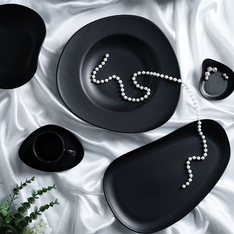 This image presents a luxurious black porcelain dinnerware set artfully arranged on a silky white fabric, creating a stunning visual contrast.