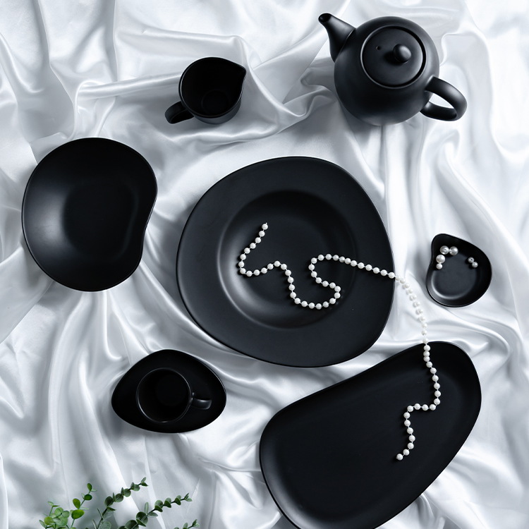 This image presents an elegant black porcelain dining ensemble, artfully arranged on a luxurious white fabric backdrop.