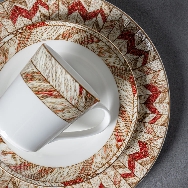 This image presents a harmonious arrangement of a cup and plate, both featuring the same intricate red and gold pattern.