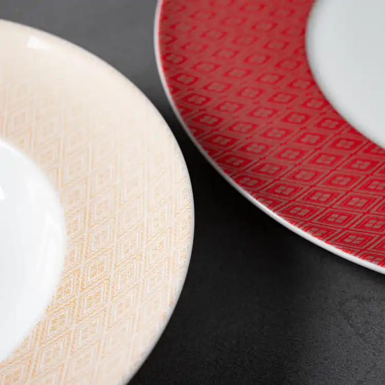 The image focuses on the detailed patterns of the dinnerware, showcasing the intricate designs of both the red and beige pieces.