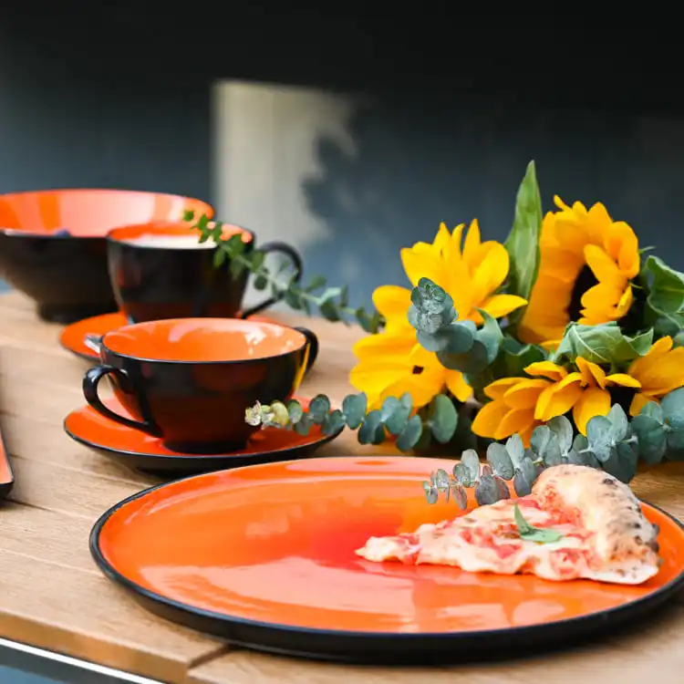 This image features a beautifully arranged table setting with orange color glazed porcelain dinnerware, including plates, cups, and bowls.