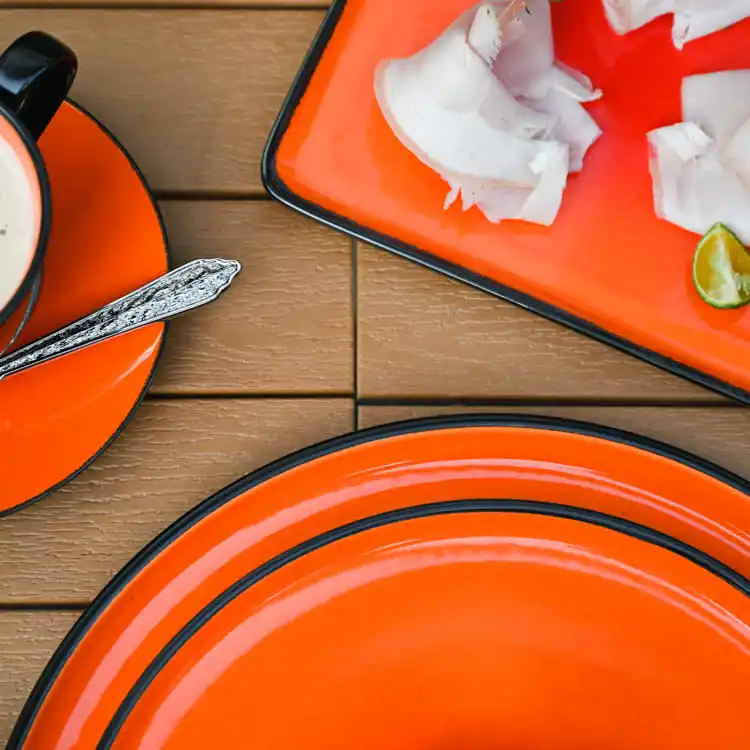 This image features a collection of orange color glazed porcelain dinnerware, including a plate, a cup with a saucer, and a rectangular platter.