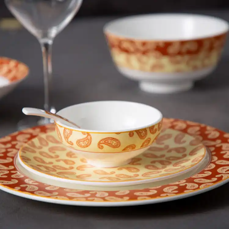 This image provides a close-up view of a porcelain bowl and plate, both featuring a detailed paisley pattern in warm orange and cream hues.