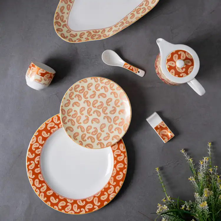 This image displays an arrangement of the paisley porcelain dinnerware set, featuring plates, a teapot, a small dish, and a spoon, all adorned with the elegant paisley pattern.