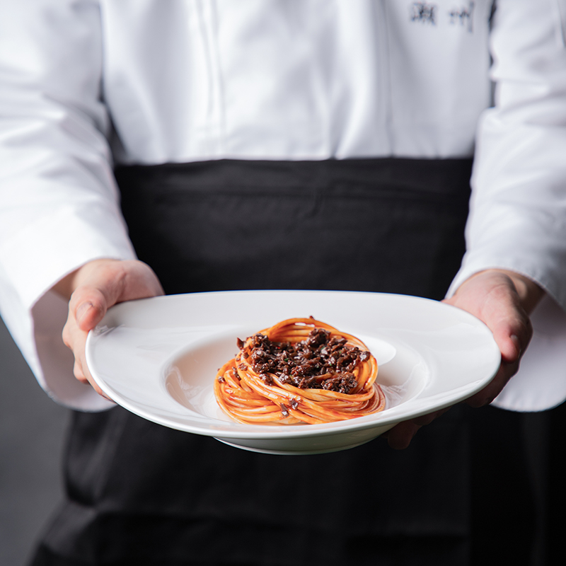 This image features a chef presenting a dish on a fine porcelain plate, highlighting the elegance and sophistication of the tableware.