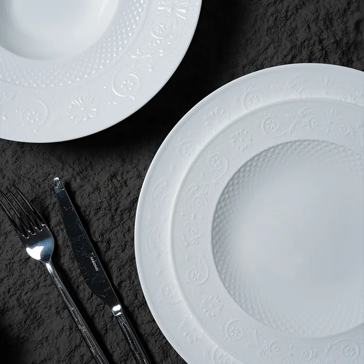 This image focuses on the detailed design of white bone china plates, emphasizing the intricate patterns and textures that adorn the dinnerware.