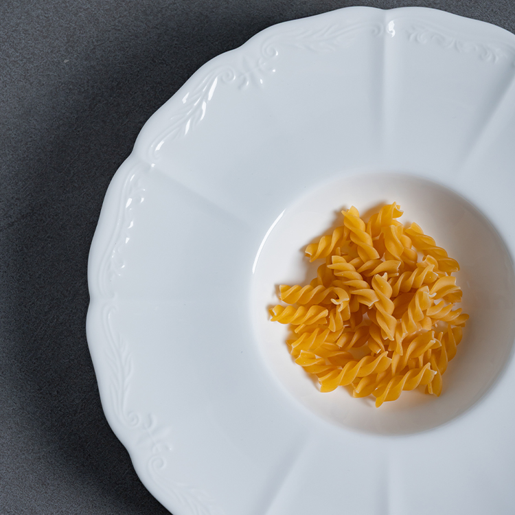 This image presents a white porcelain plate elegantly adorned with raw pasta spirals, emphasizing the simplicity and beauty of pure design.
