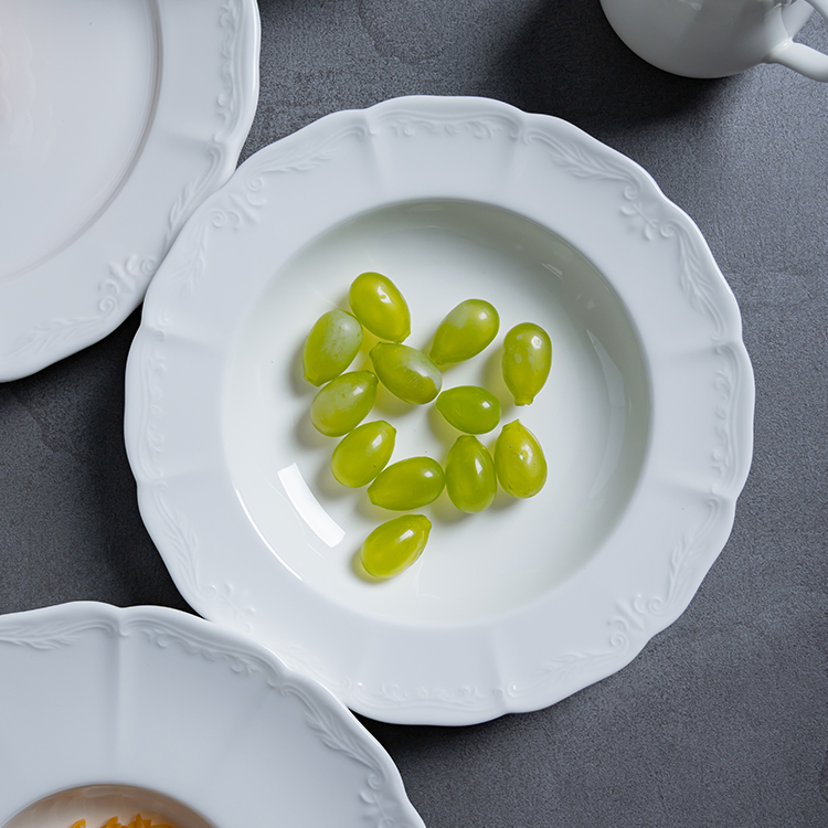 This image showcases a beautifully crafted white porcelain plate adorned with a cluster of fresh green grapes.