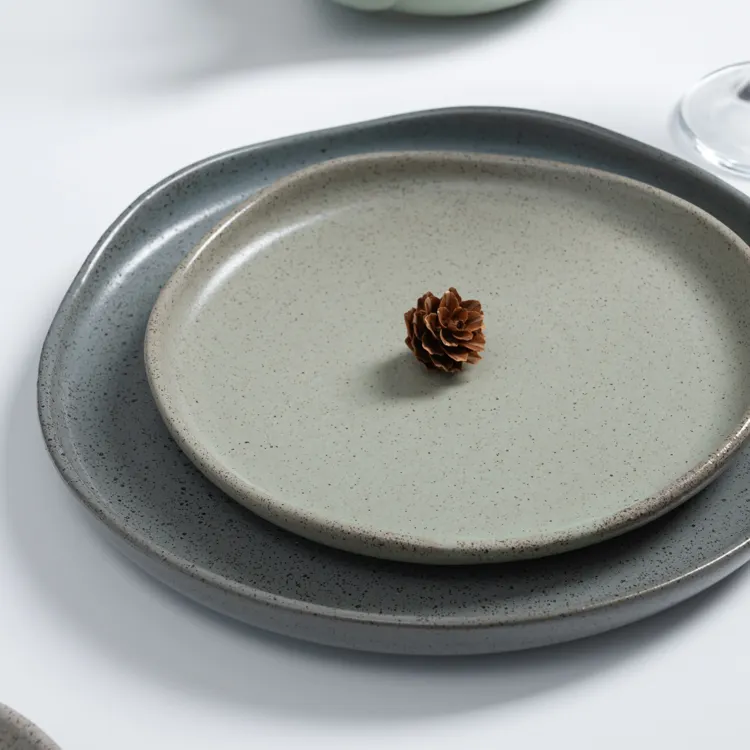 The image features a minimalist design with two porcelain plates stacked together, each with a speckled glaze in soft, neutral tones.
