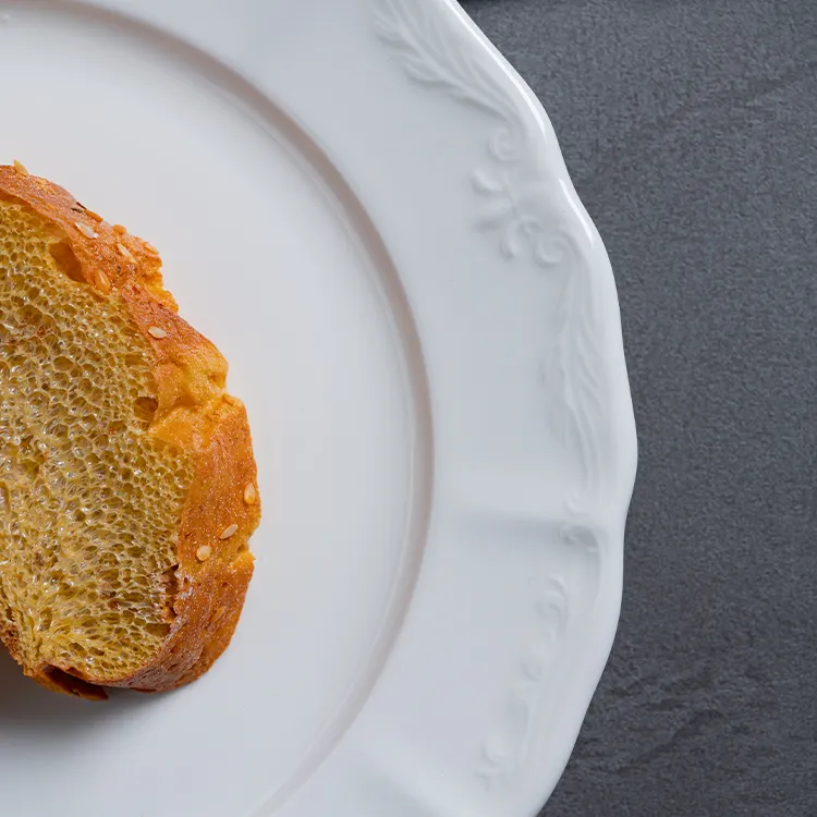 This image captures a close-up view of a fine porcelain plate with a piece of artisanal bread placed on it.