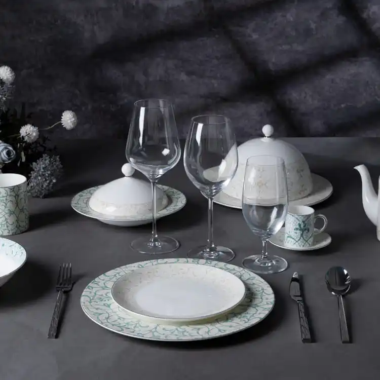 This image depicts a sophisticated dining setup featuring a complete floral dinnerware collection, including plates, cups, saucers, and glassware, all arranged elegantly on a dark table.