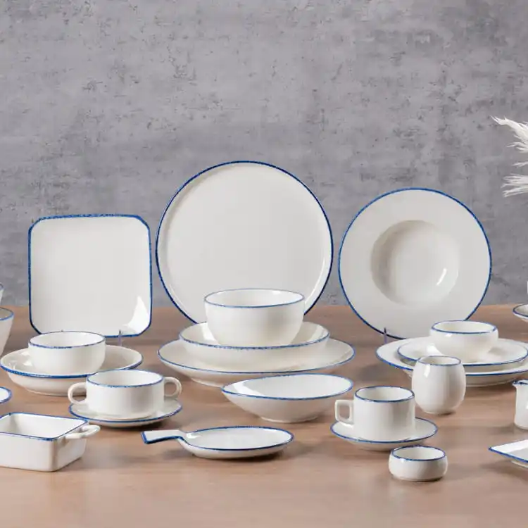 This image displays a comprehensive collection of modern white porcelain dinnerware, arranged against a neutral background. The set includes a variety of plates, bowls, cups, and serving dishes, each featuring a subtle blue rim that adds a touch of elegance.