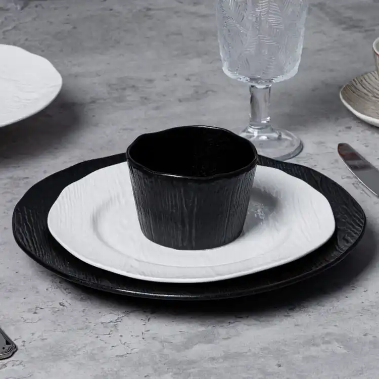 The central focus is a black cup placed on a white plate, which is further set on a larger black plate.