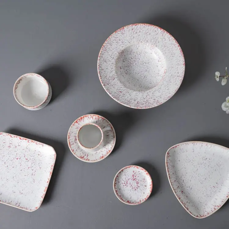 The set includes a variety of shapes such as a round bowl, a small cup, a saucer, and a rectangular plate, each adorned with a delicate pink speckle pattern.