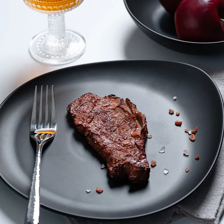 This image features a beautifully cooked steak presented on an irregularly shaped black porcelain plate.