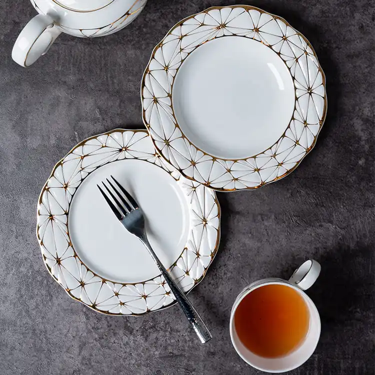This image presents a sophisticated dining setup featuring two bone china plates with a gold rim, a teapot, and a cup of tea.