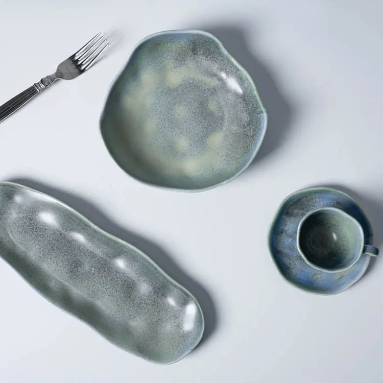 Esta imagen muestra un trío de piezas de vajilla de porcelana azul verdosa, que incluye un tazón, una taza y una fuente larga para servir, complementadas con un tenedor.