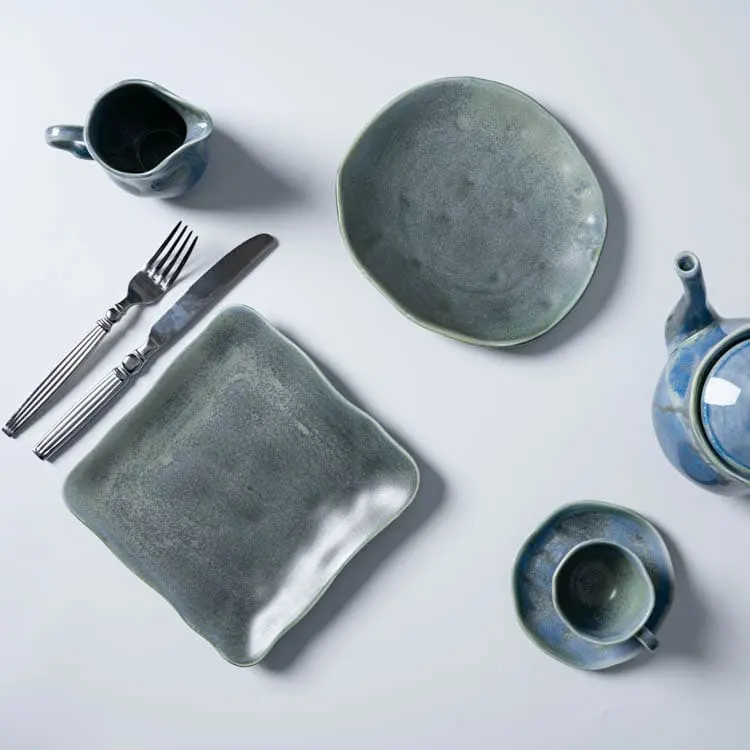 Esta imagen muestra una selección de vajilla de porcelana azul verdosa, que incluye un plato, una taza, una tetera y una jarra pequeña, dispuestos junto a un cuchillo y un tenedor.