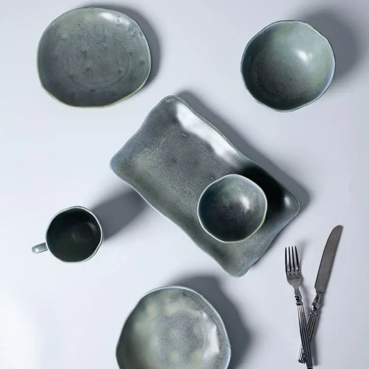 Esta imagen presenta una variedad de piezas de vajilla de porcelana azul verdosa, incluidos cuencos, platos y una taza, dispuestos junto a un cuchillo y un tenedor.