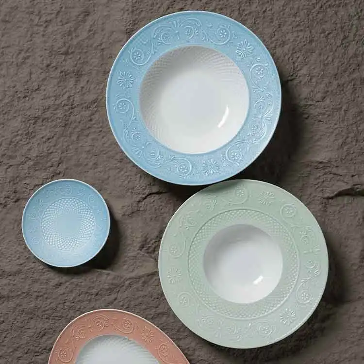 Pastel bone china embossed plates in blue, green, and pink with floral rims on a dark gray textured stone background.