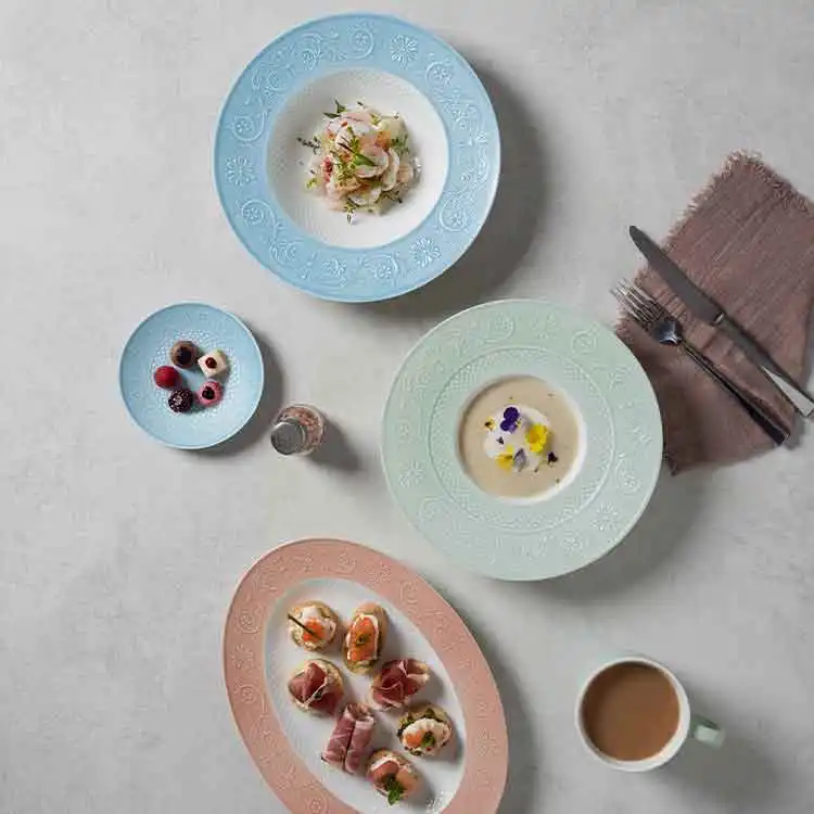 Top-down view of bone china embossed plates with assorted appetizers, unified pastel table setting showcasing consistent plating standard for chain restaurants.