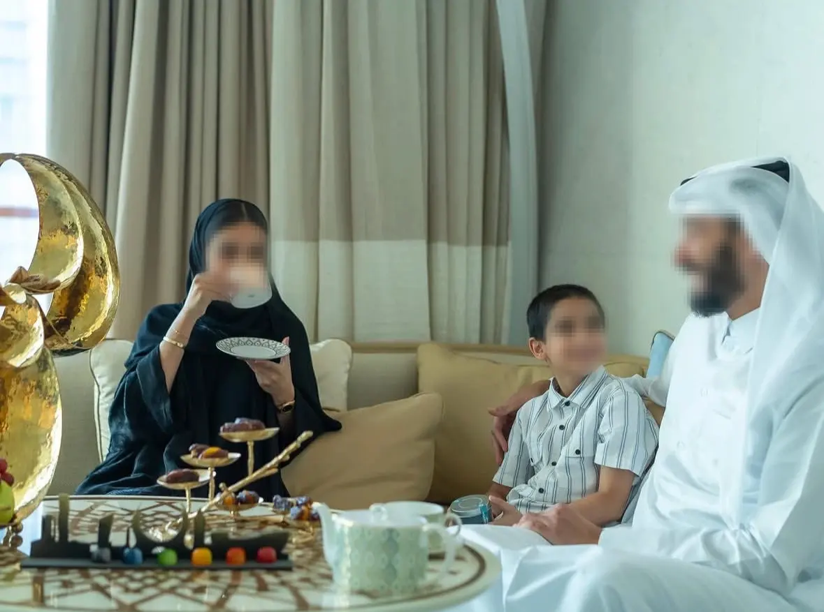Middle Eastern family relaxing in hotel room, enjoying tea with custom patterned bone china tableware and fruit dessert stands on decorative coffee table.