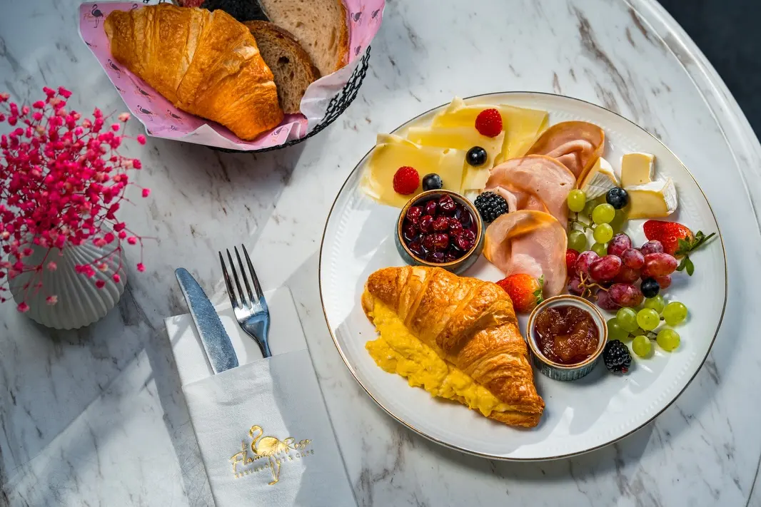 Breakfast platter with scrambled egg croissant, ham, cheese, and fresh fruit on a gold rim plate.