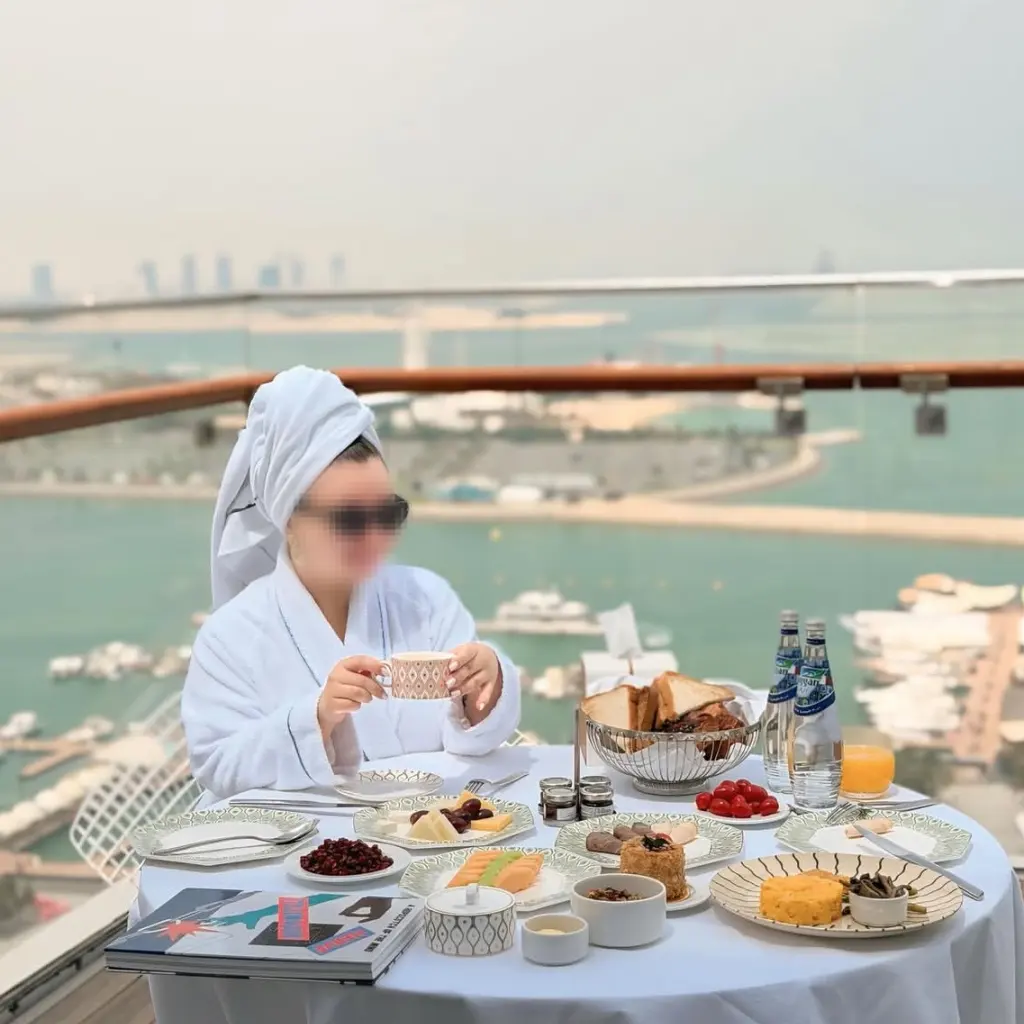 Guest in bathrobe enjoys private balcony breakfast with sea city view at Fairmont Doha, all food served on exclusive custom bone china for premium in-room dining service.