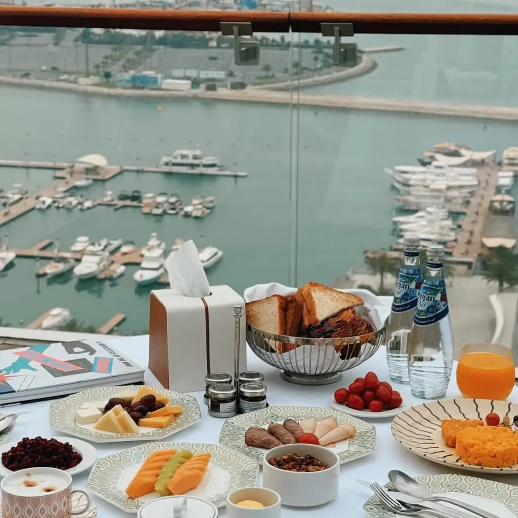 Abundant private balcony breakfast spread at Fairmont Doha with yacht harbor sea view, all food served on hotel exclusive custom bone china for premium in-room dining experience.