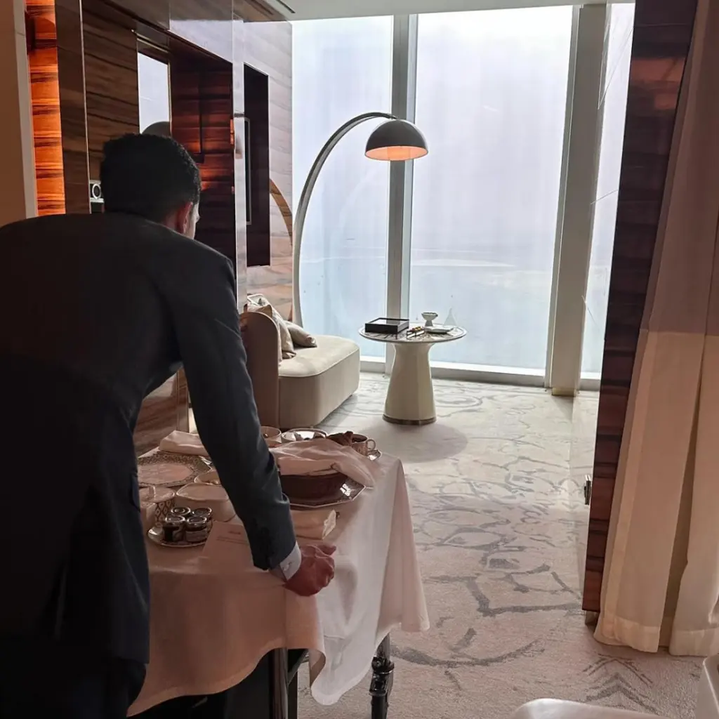 Hotel staff arranges in-room dining trolley with exclusive custom bone china tableware for Fairmont Doha, delivering private personalized guest dining service in suite.