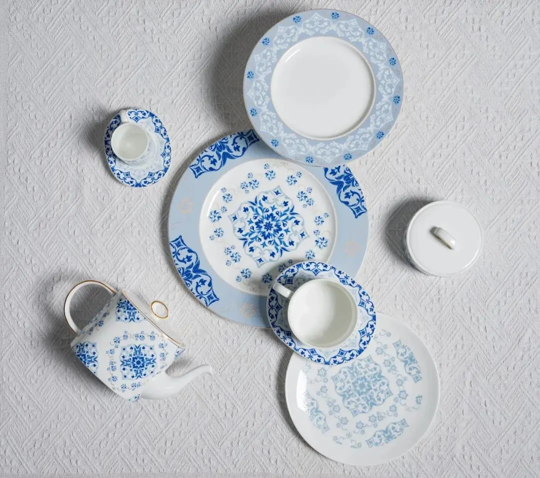 Overhead view of blue and white porcelain dinnerware set with plates, cups, and teapot on textured white surface