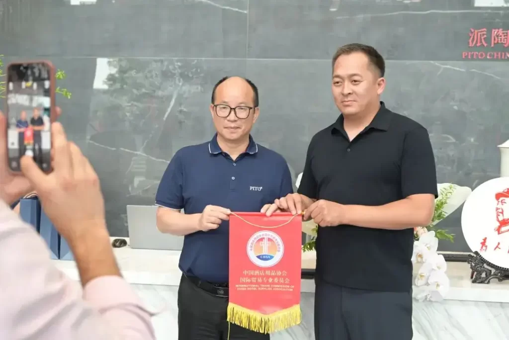 PITO representative presents a CHSA pennant to the Kyrgyz official; another person takes a photo.