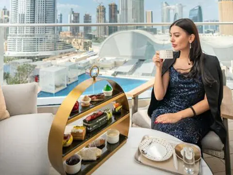 A woman drinks from a cup during high tea on a balcony with a city view.